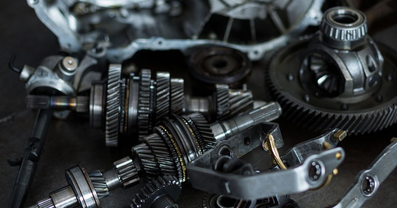 Componenti meccanici di precisione per automotive, tra cui ingranaggi, alberi e parti metalliche, su un piano di lavoro in un'officina meccanica.