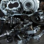 Componenti meccanici di precisione per automotive, tra cui ingranaggi, alberi e parti metalliche, su un piano di lavoro in un'officina meccanica.