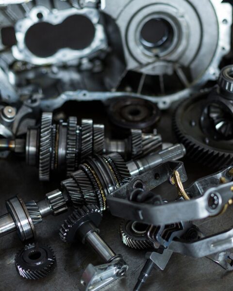 Componenti meccanici di precisione per automotive, tra cui ingranaggi, alberi e parti metalliche, su un piano di lavoro in un'officina meccanica.