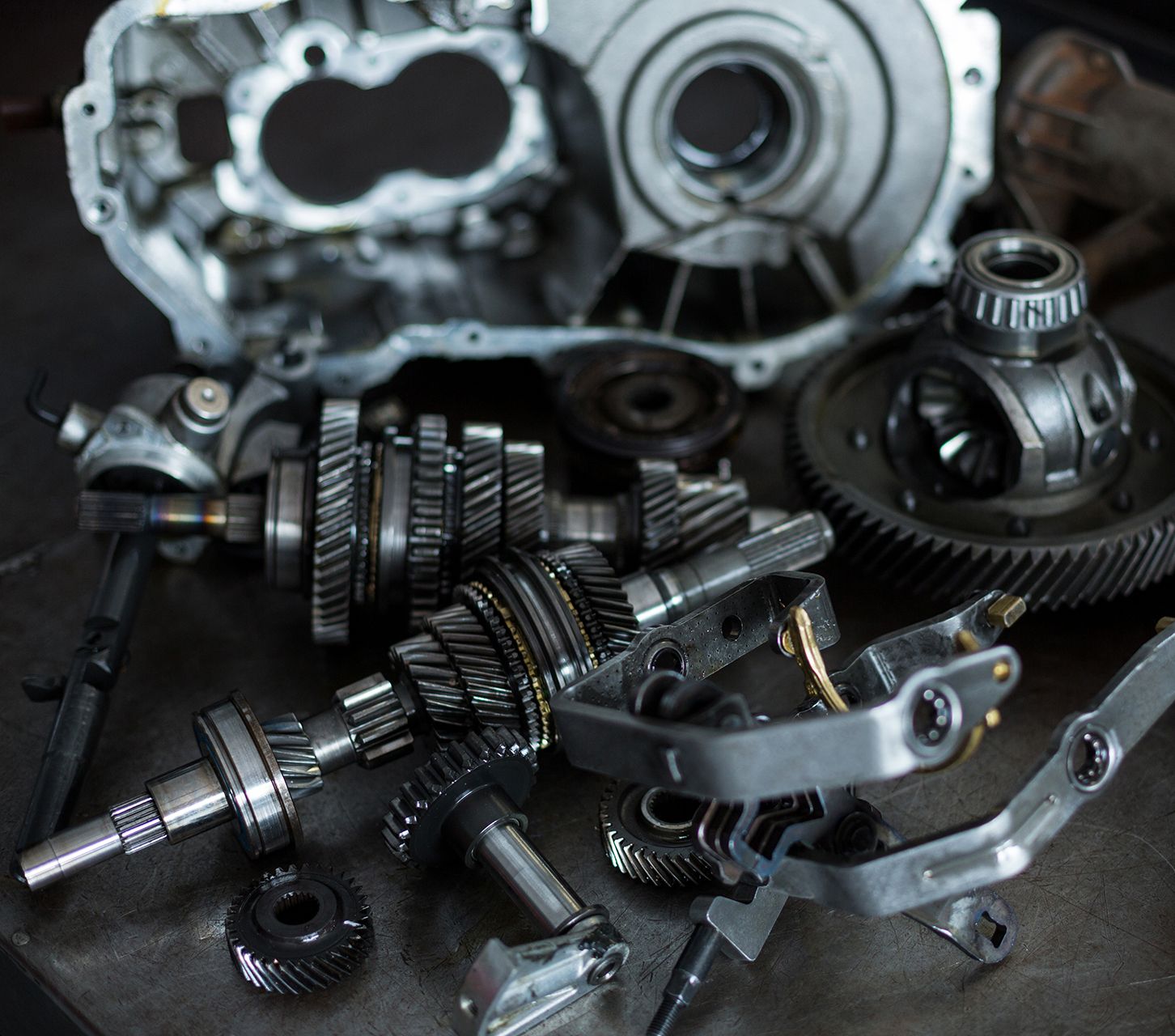 Componenti meccanici di precisione per automotive, tra cui ingranaggi, alberi e parti metalliche, su un piano di lavoro in un'officina meccanica.