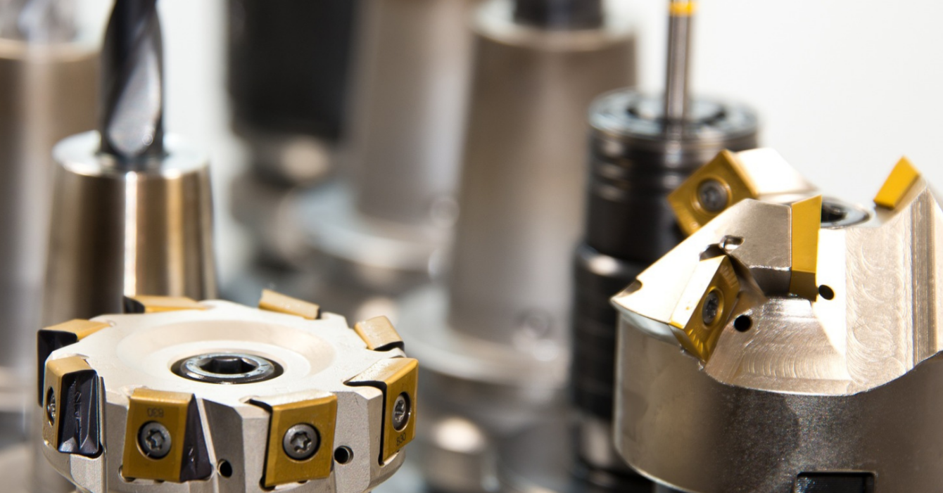 L'immagine mostra diversi utensili da taglio per macchine CNC, tra cui frese e punte, disposti in fila. Questi strumenti sono usati in lavorazioni meccaniche di precisione, come fresatura e foratura, per modellare e lavorare materiali come metallo o plastica. Gli utensili hanno superfici lucide e affilate, alcuni con inserti di colore giallo, tipici degli utensili in metallo duro utilizzati per tagli ad alta velocità.