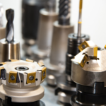L'immagine mostra diversi utensili da taglio per macchine CNC, tra cui frese e punte, disposti in fila. Questi strumenti sono usati in lavorazioni meccaniche di precisione, come fresatura e foratura, per modellare e lavorare materiali come metallo o plastica. Gli utensili hanno superfici lucide e affilate, alcuni con inserti di colore giallo, tipici degli utensili in metallo duro utilizzati per tagli ad alta velocità.