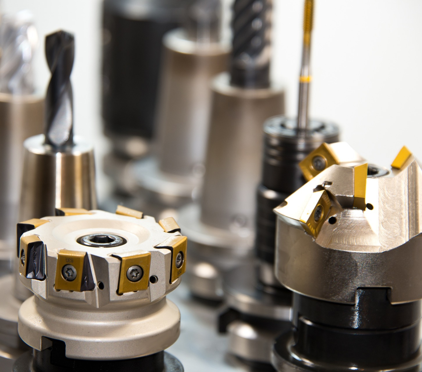 L'immagine mostra diversi utensili da taglio per macchine CNC, tra cui frese e punte, disposti in fila. Questi strumenti sono usati in lavorazioni meccaniche di precisione, come fresatura e foratura, per modellare e lavorare materiali come metallo o plastica. Gli utensili hanno superfici lucide e affilate, alcuni con inserti di colore giallo, tipici degli utensili in metallo duro utilizzati per tagli ad alta velocità.