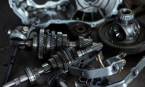 Componenti meccanici di precisione per automotive, tra cui ingranaggi, alberi e parti metalliche, su un piano di lavoro in un'officina meccanica.